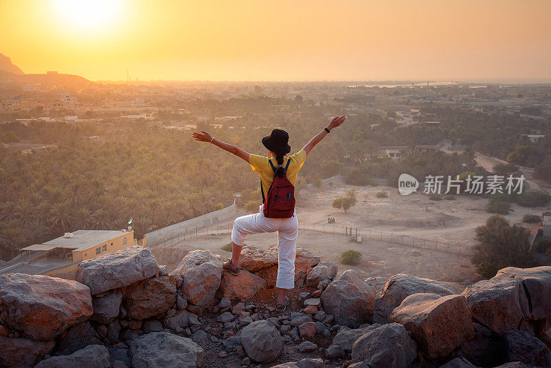 在日落时分的阿联酋沙漠山，一名女子欣赏山顶的景色