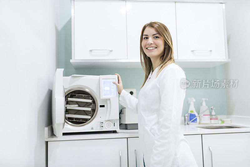 一位穿着实验服的女牙医在高压釜旁微笑着看着摄像机