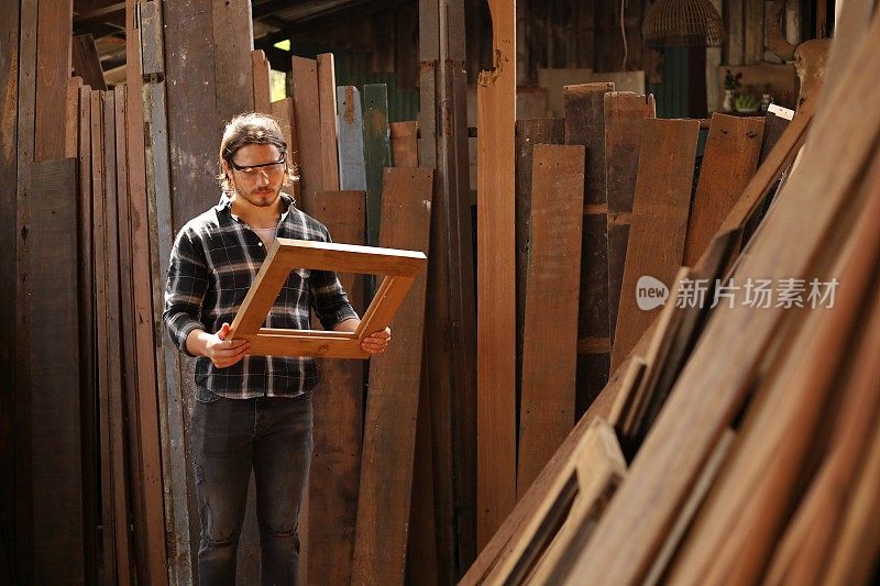 年轻的白人木匠正在他自己的车库风格的车间里做木制框架的爱好