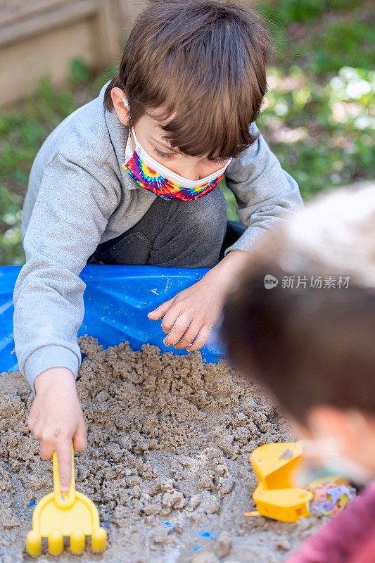 小男孩们戴着防护面具在学前学校的操场上玩耍