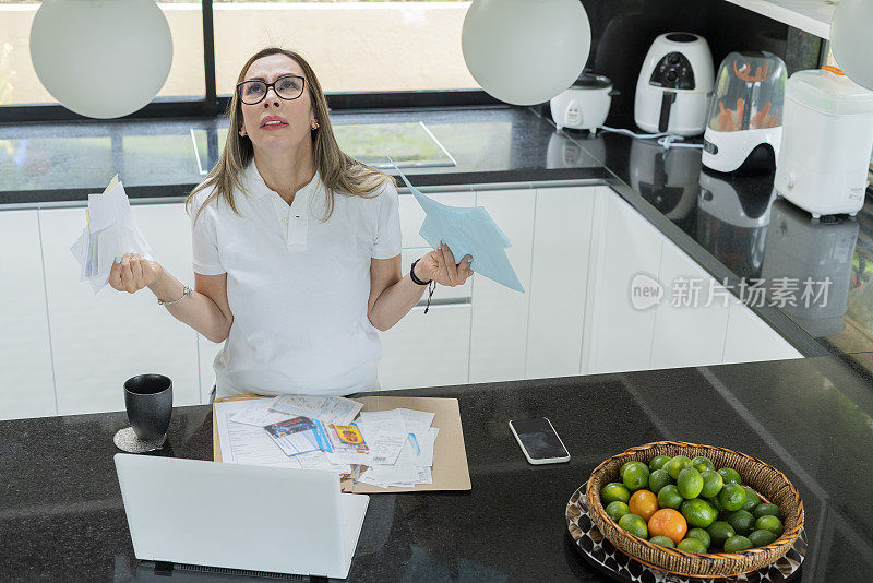 一名妇女穿着舒适的衣服，在厨房里用笔记本电脑查看她的财务状况