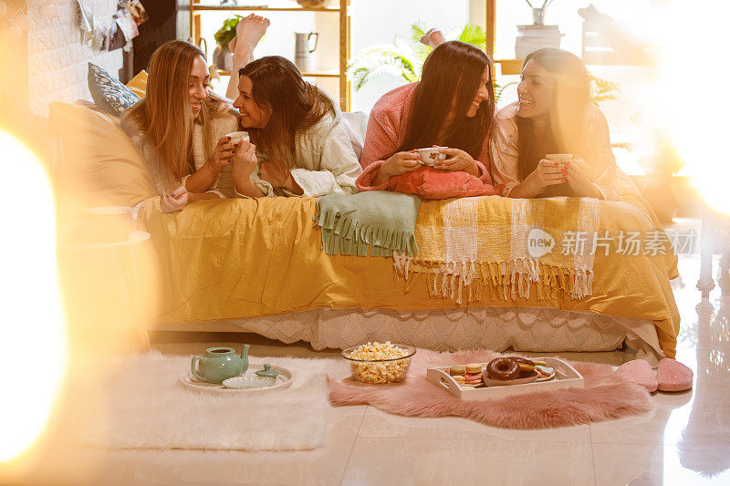 四个女朋友在床上放松，享受着茶和零食