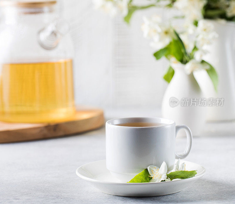 一杯茉莉花绿茶背景是一个茶壶和一枝茉莉花。