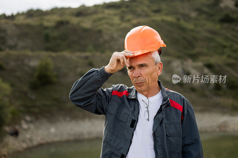 一位高级男工程师的肖像，他正在纠正他头上的橙色头盔