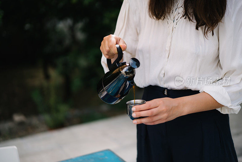 一个年轻的女人把咖啡倒进花园的杯子里