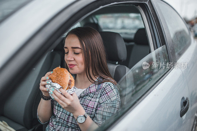 一个微笑的女人在车里吃汉堡包