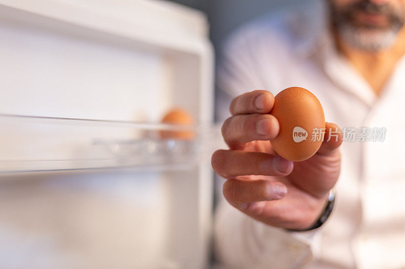男性的手在冰箱门旁拿着一个鸡蛋。背景中的物体焦距不清