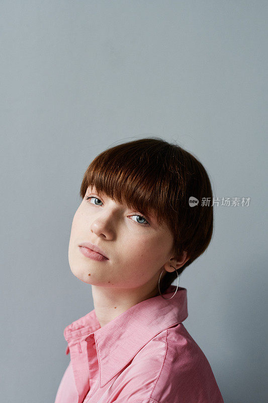 一幅画描绘的是一个平静美丽的女孩，戴着耳环，身穿粉色衬衫，靠在灰色的墙上