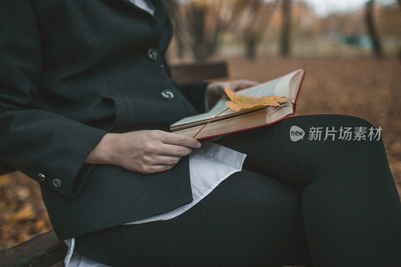一个女人拿着一本书坐在长凳上，脸看不见
