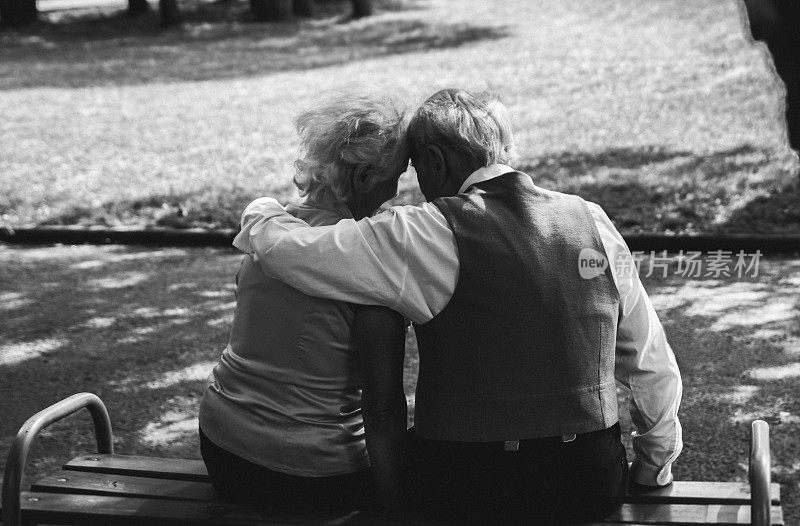 一对老夫妇坐在公园里的长凳上。祖母和祖父在他们的金婚纪念日上。五十年在一起。老人在黑白照片上拥抱。