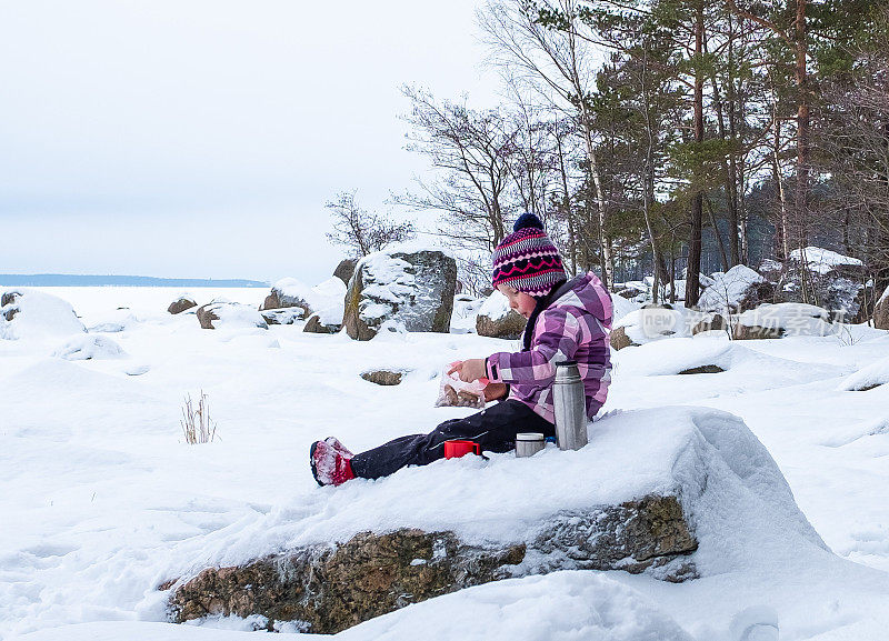 快乐的4岁女孩，白人孩子，在冬天的大自然中吃零食。