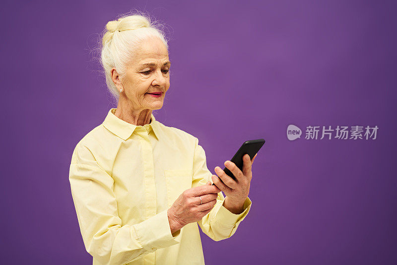 身穿黄色衬衫的高级妇女一边发短信一边看着智能手机屏幕