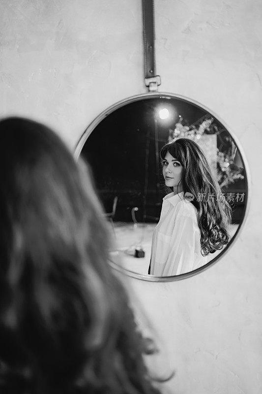 一个穿白衬衫的女人看着一面圆镜中的倒影。黑白两色