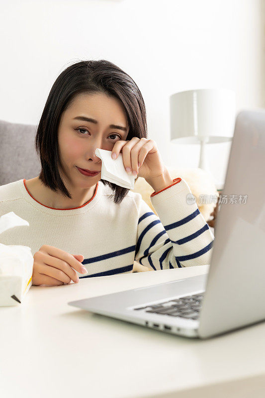 年轻漂亮的亚洲女人坐在客厅舒适的沙发上，同时使用她的笔记本电脑。