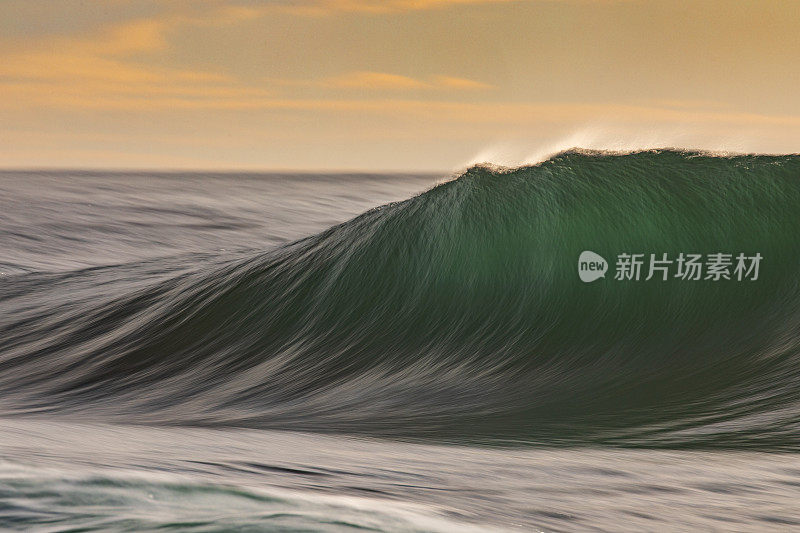 平滑的海浪在清晨形成金色的光和戏剧性的天空在日出