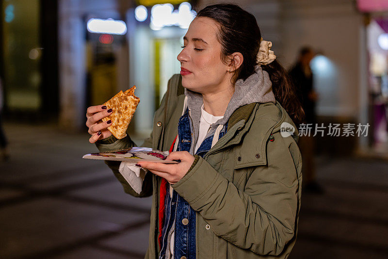 一个凉爽的夜晚，年轻女子享用着一片披萨