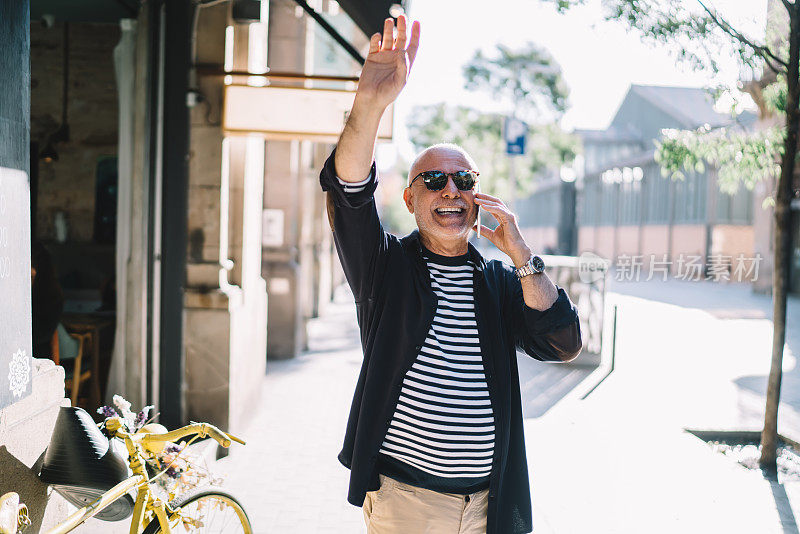 有趣的男性游客用手机设备上的漫游互联网连接讨论退休后的国际假期，开朗的老人在城市里挥手大笑，同时通过手机打电话