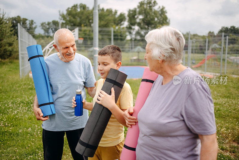 老人和孙子抱着运动垫站在公园里的照片