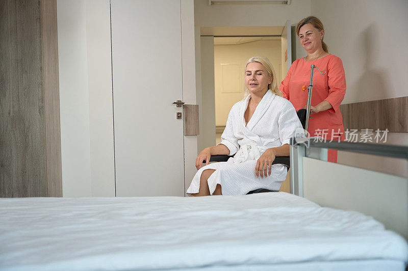 细心的护士把一个坐着轮椅的病人抬进病房