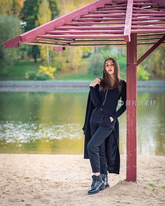 一个美丽的女孩在秋天的公园里撑着伞站在池塘边。