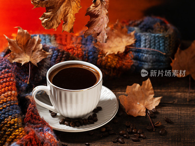 木桌上的一杯黑咖啡。秋天干枫叶和织围巾。桌上的咖啡豆
