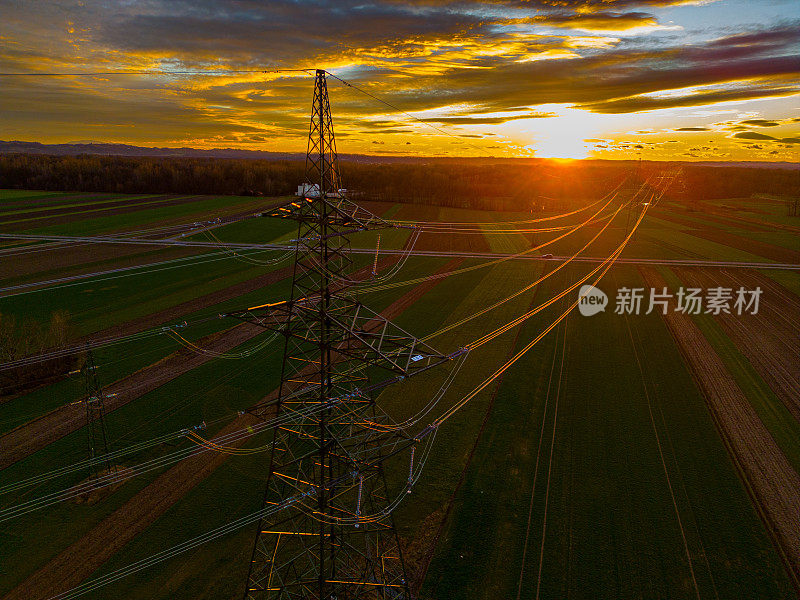 鸟瞰图夕阳下绿色农田上的高压电线和电塔