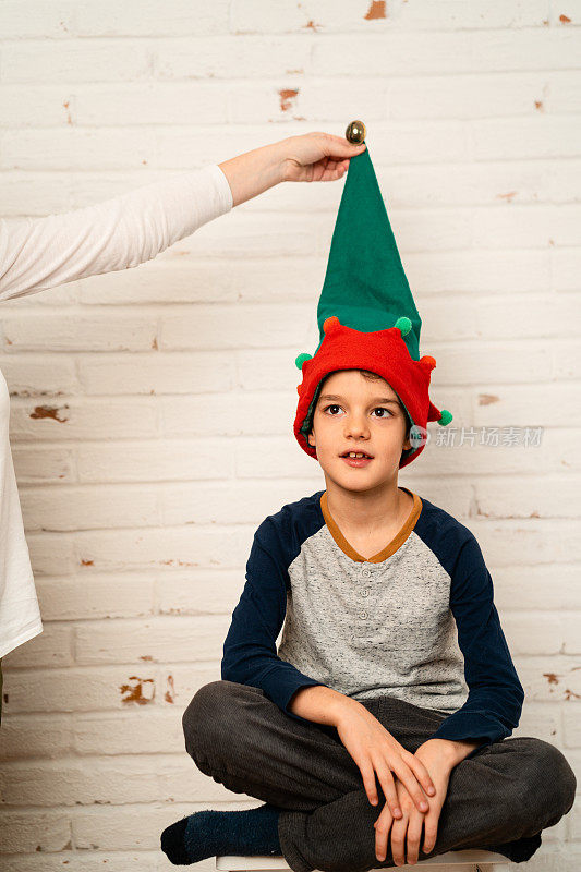 小男孩戴着圣诞精灵帽在白色砖墙前摆姿势