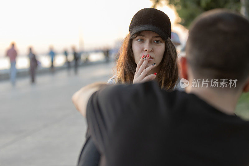 年轻女子一边抽烟一边和她的男朋友聊天。