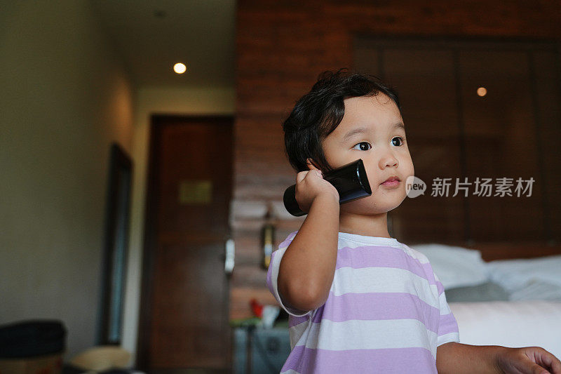拿着电视遥控器的亚洲男婴在客厅里用临时电话胡言乱语