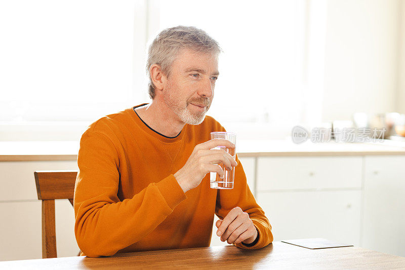 一位50岁的老人在自家厨房用玻璃杯喝水