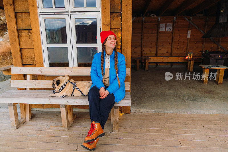 挪威，一个快乐的女人带着一只狗，头戴红帽，在山上欣赏冬天的时光