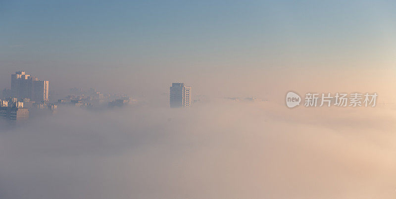 晨雾笼罩着城市。浓雾笼罩着住宅区。建筑物从雾中伸出来。广泛的全景。