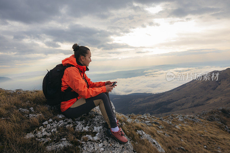 美丽的女徒步旅行者坐在山顶的岩石上