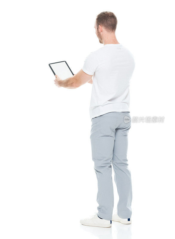 白人男性穿着裤子站在白色背景前使用平板电脑