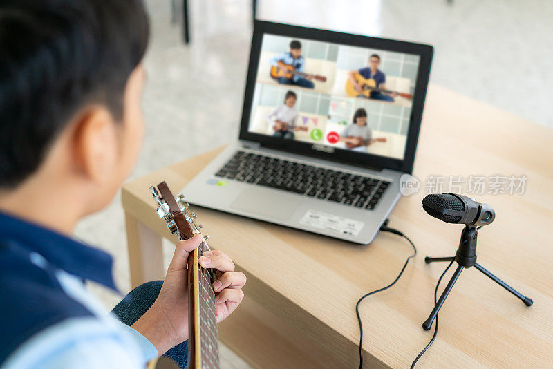 亚洲男孩弹奏吉他虚拟快乐时间会议在网上玩音乐与朋友在视频会议与笔记本电脑在网上会议在视频通话为社会距离。