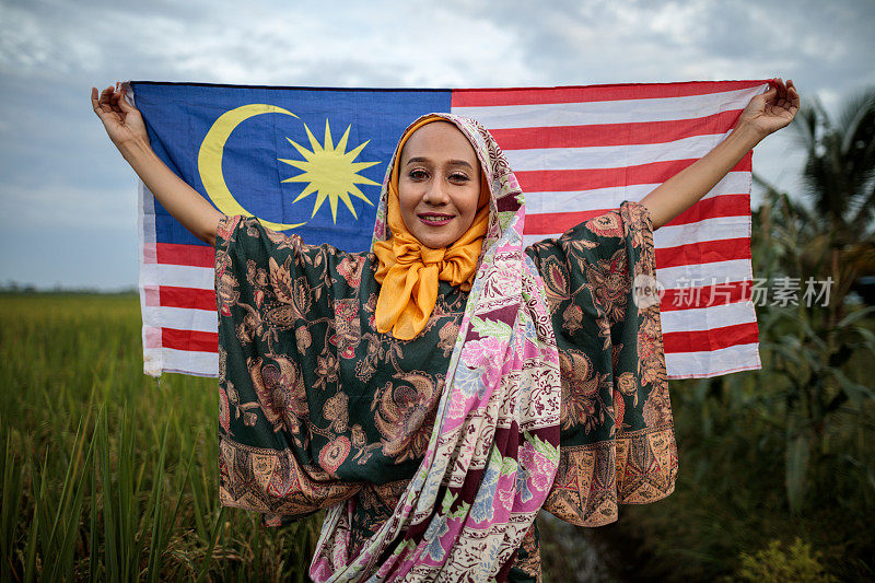 年轻的亚洲妇女在稻田里挥舞着马来西亚国旗