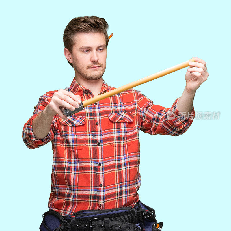 男性建筑承包商站在蓝色背景，穿着伐木工衬衫，拿着锤子和使用卷尺