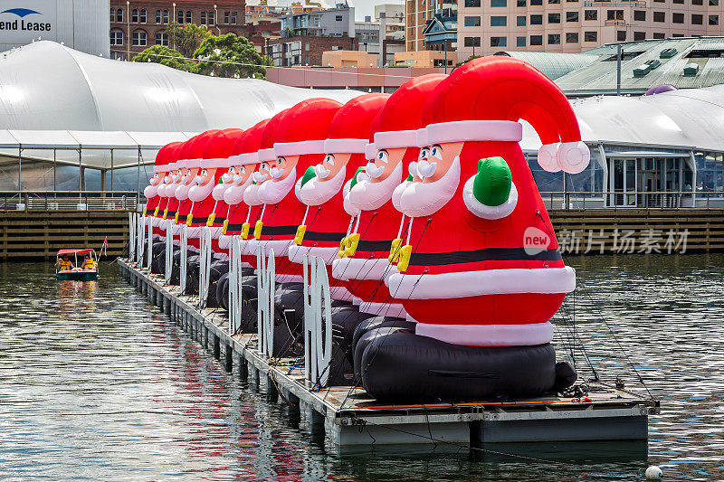 澳大利亚新南威尔士州悉尼，一排巨大的充气圣诞老人漂浮在达令港