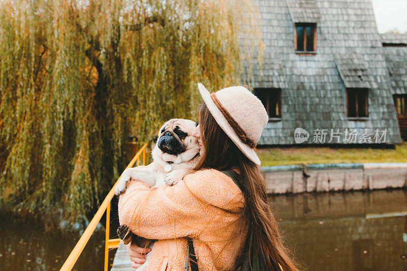 戴着帽子的女人和一只狗在美丽的木屋湖边散步，遇见了秋天