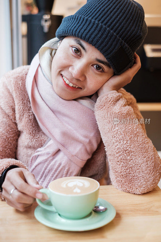 快乐的女人与毛衣享受在咖啡馆喝热咖啡