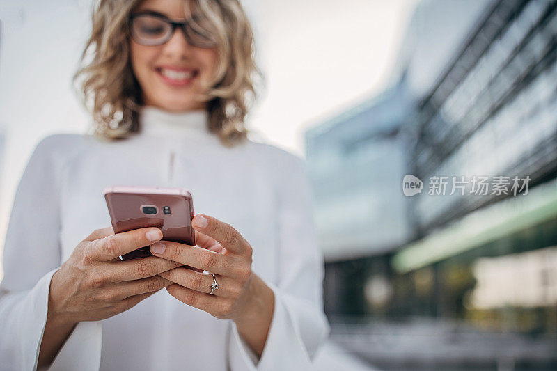 一位年轻的女商人在户外用智能手机发短信