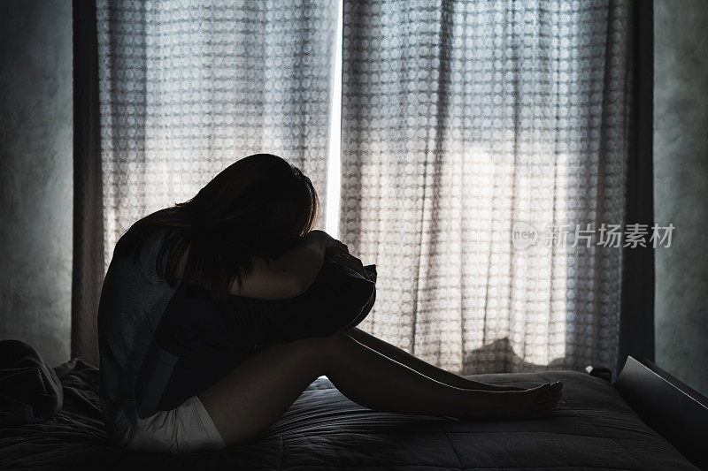 孤独的年轻女人沮丧和压力坐在黑暗的卧室里，消极情绪的概念