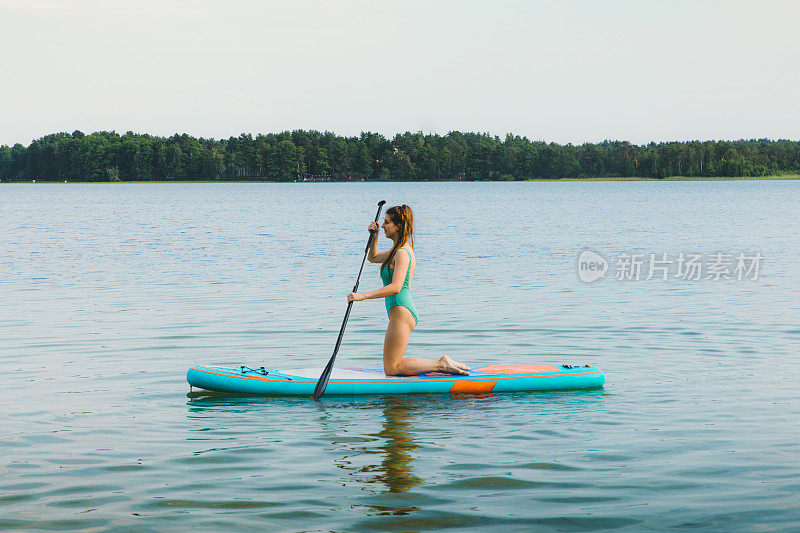 年轻女子欣赏美丽的夏日日落在湖上划水