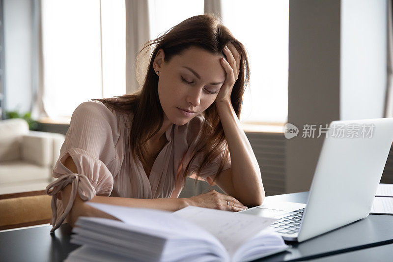 疲惫困倦的女人坐在书桌上，抱着头，手提电脑