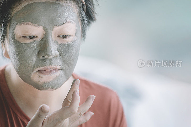 一位亚洲华人中年女性正在准备化妆，在家里脸部水疗，纵容自己的粘土面膜皮肤护理