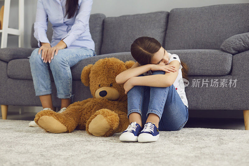 伤心被冒犯的孩子坐在地板上不与母亲在房间里说话。
