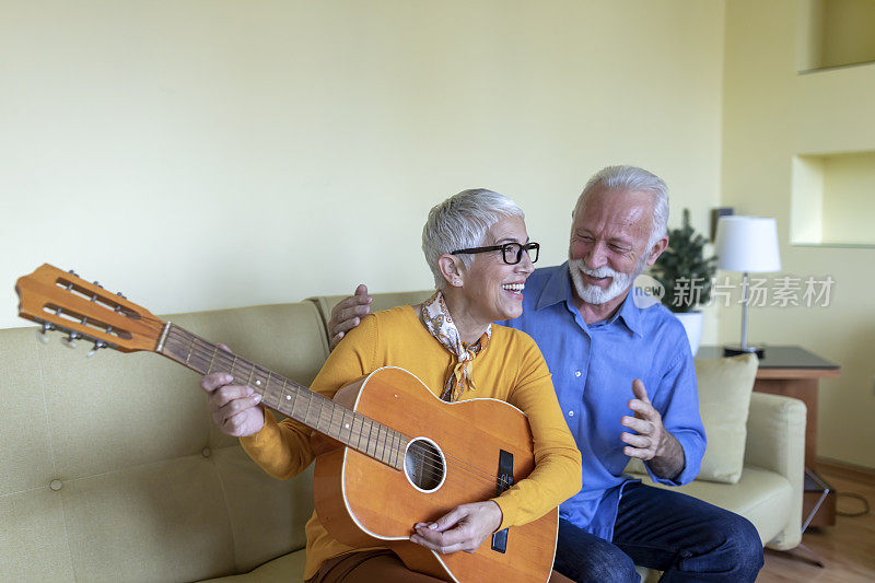 一位快乐的退休老人正在为她喜欢轻松音乐的英俊的丈夫弹吉他。