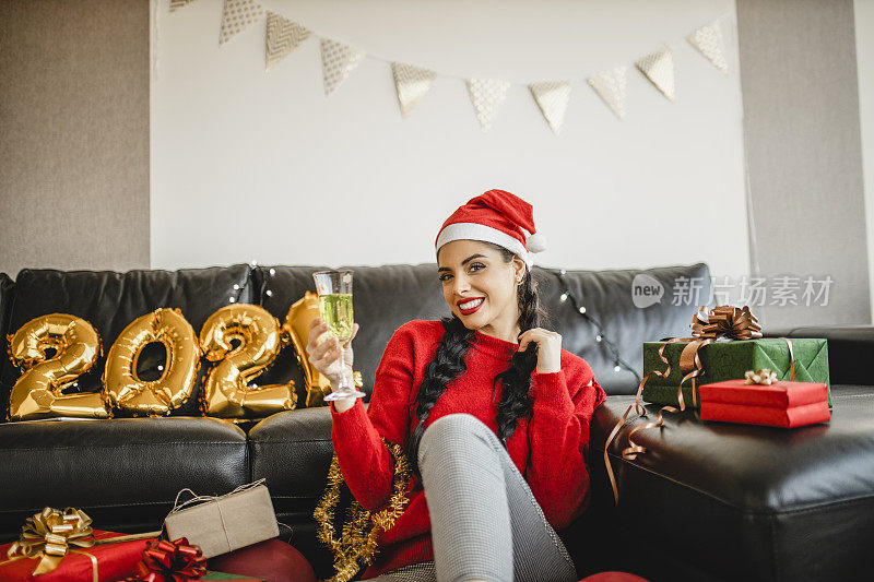 穿着红毛衣在家喝香槟庆祝新年的女人