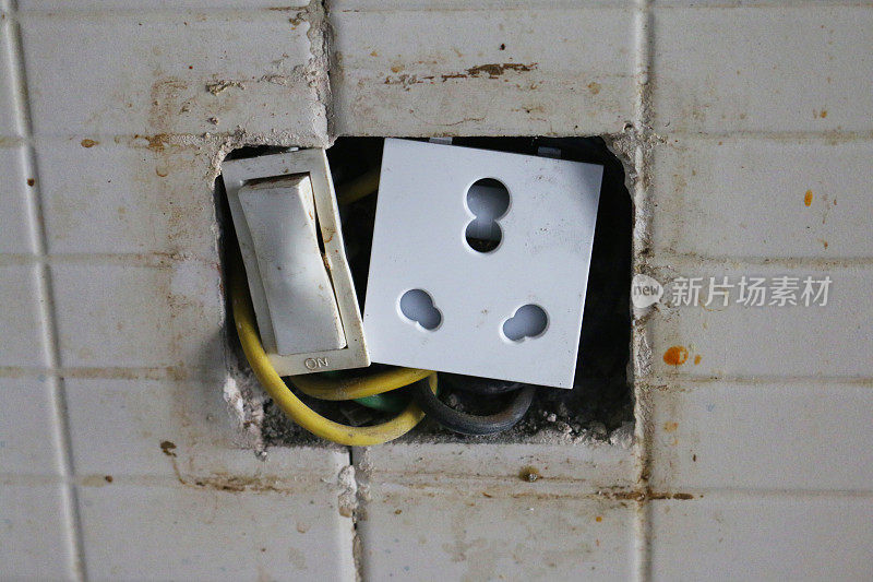 在肮脏的，白色瓷砖墙上的洞的特写图像与危险的电源插座和塑料涂层电线，电气危险