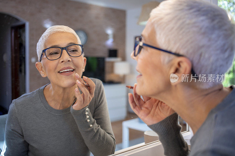 美丽成熟的女人看着镜子里的自己，涂上口红眼线。